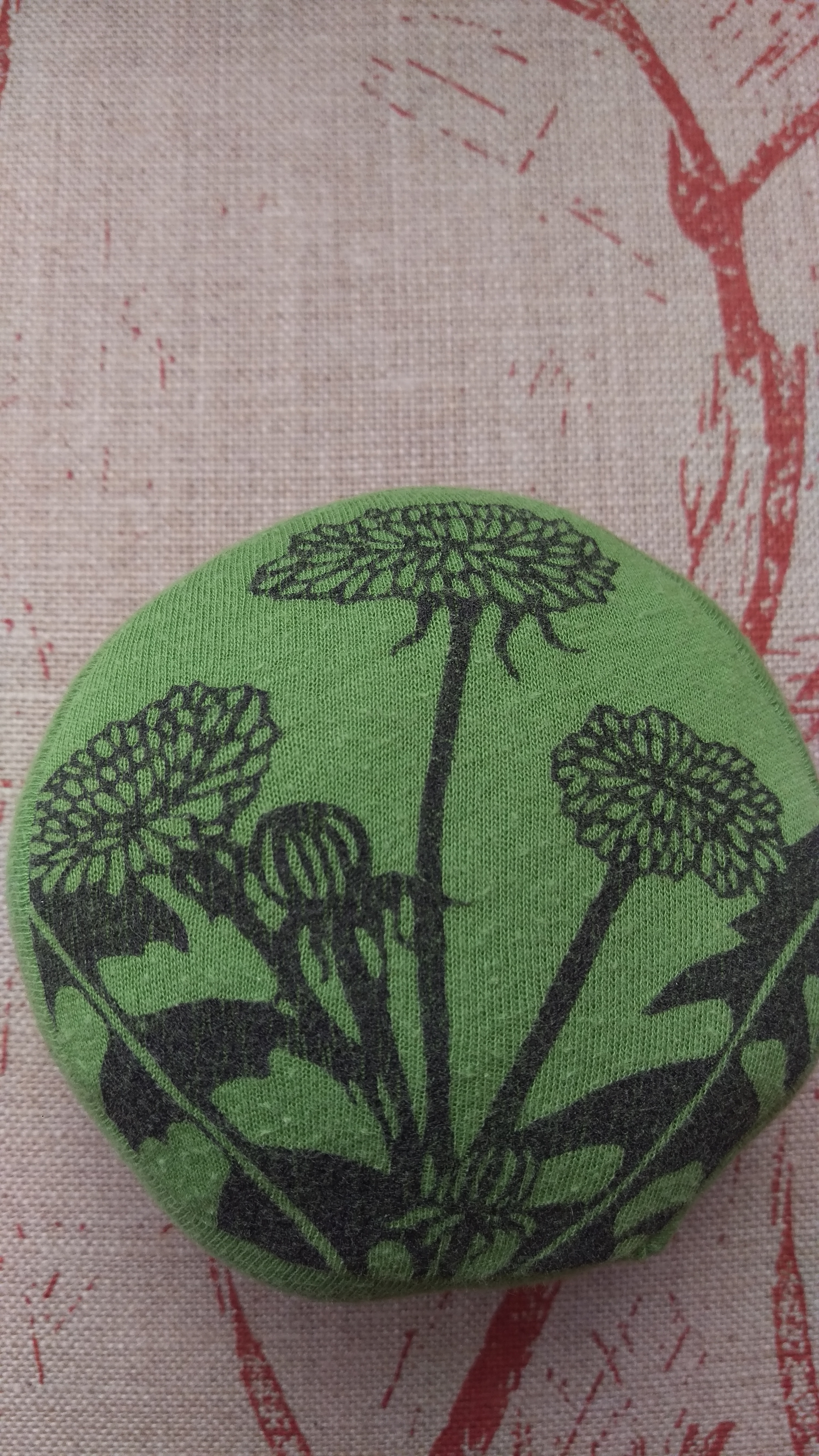 Small round green cushion with design of a dandelion in black