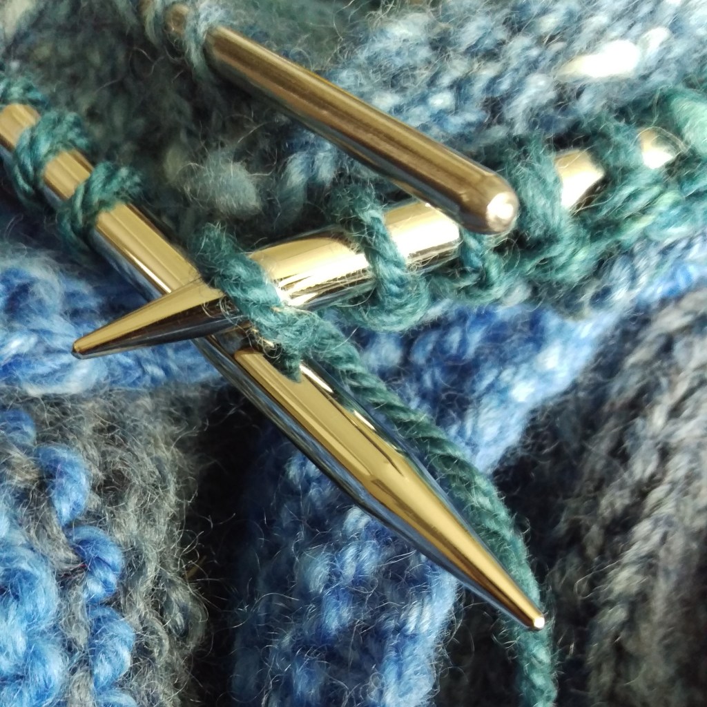 Lots of blue knitting with live stitches on steel circulars and a blunt ended steel chopstick. Three needle bind off in progress. 